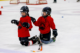 Two girls in hockey gear smiling while kneeling on an ice rink